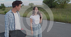 Couple of teens walking with skateboard on a road out of city and having fun