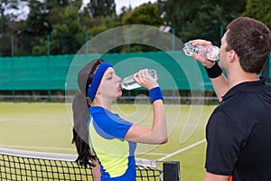 Couple of tennis players drinking water after match outdoor