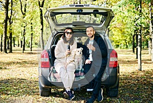 Couple with their dog relaxing in forest sitting in car trunk