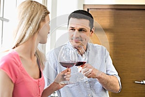 Couple toasting red wine glasses in kitchen