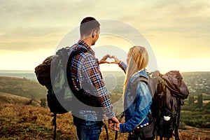 A couple of tourists with backpacks made a symbol of the heart w