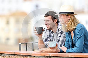 Couple of tourists drinking coffee and looking away in a balcony