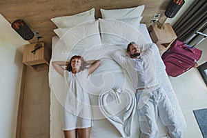 couple of tourists in hotel room relaxing and smiling on the bed, top view