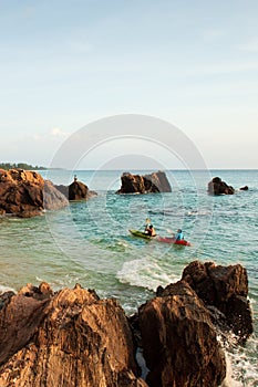 Couple tourists kayaking in tropical sea in the evening. Beautiful bay, stone, rocks and waves. Fishermen and sunset sky