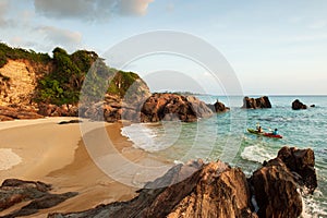 Couple tourists kayaking in tropical sea in the evening. Beautiful curved bay, beach, stone, rocks and waves. Fishermen and sunset