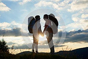 Couple of tourists in love with backpacks facing each other at sunset in the mountains