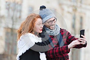 Couple of tourists makes selfy on smart-phone. Man and woman looking for city map in telephone. Urban couple make video chatting.