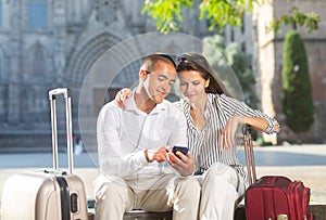 Couple of tourists resting on bench, consulting navigation app in cellphone