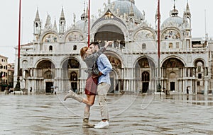 Couple of tourists visiting Venice, Italy - Boyfriend and girlfriend kissing under the rain on city street at sunset