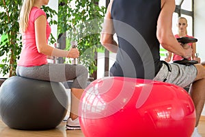 Couple training in gym with dumbbells in front of a mirror sitting on fitballs