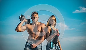 Couple training outdoors, sport and health concept. Man with muscular torso and blond smiling girl lifting dumbbells