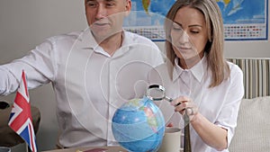 A couple in a travel agency, a girl with a magnifying glass looks at a globe.