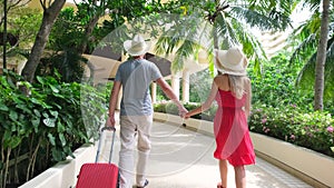 Couple traveler man and woman girl in red dress with suitcase at luxury resort