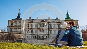 Couple of travelers relaxes enjoying view of Pidhirtsi castle. Ancient architecture landmark. Tourism in Westerm Ukraine