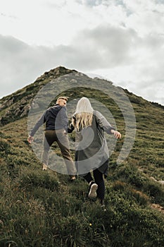 Couple travelers woman and man follow holding hands at mountains with landscape on background. happy emotions