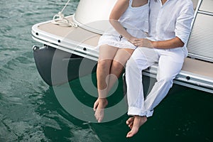 Couple is traveling on a yacht in the Indian ocean. Man and a woman sit on the edge of the boat.