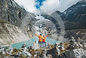 Couple trekkers dressed bright jackets on the rock enjoying a glacier falling in high altitude Sabai Tso glacial lake cca 4350m.