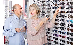 Couple trying spectacles frames and smiling near stand