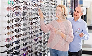 Couple trying spectacles frames and smiling near stand