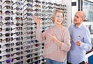 Couple trying spectacles frames and smiling near stand