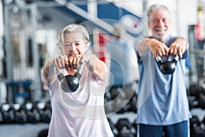 Couple of two active and healthy seniors or pensioners or mature people doinng exercise together in the gym holding a dumbbell in