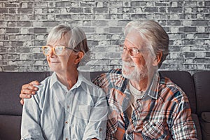 Couple of two beautiful and cute seniors at home sitting on the sofa looking at the window wearing glasses together