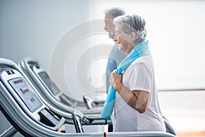 Couple of two happy and fitess seniors doing exercise in the gym together running on the tapis roulant - active lifestyle