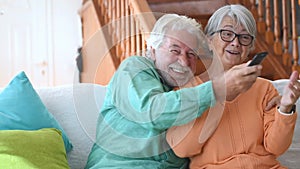 Couple of two happy seniors cooking together in the kitchen learning and following a video tutorial of cook in the laptop -