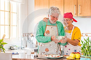 Couple of two happy seniors having fun and cooking together in the kitchen of their home - preparing some healthy food with