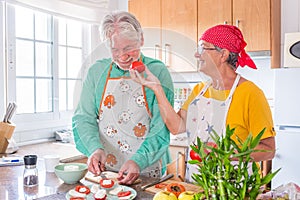 Couple of two happy seniors having fun and cooking together in the kitchen of their home - preparing some healthy food with