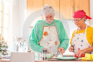 Couple of two happy seniors having fun and cooking together in the kitchen of their home - preparing some healthy food with