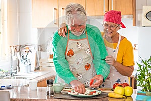 Couple of two happy seniors having fun and cooking together in the kitchen of their home - preparing some healthy food with