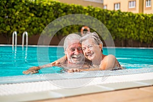 Couple of two happy seniors having fun and enjoying together in the swimming pool smiling and playing. Happy people enjoying