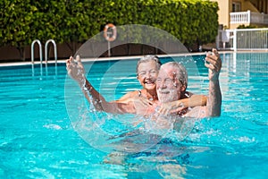 Couple of two happy seniors having fun and enjoying together in the swimming pool smiling and playing. Happy people enjoying