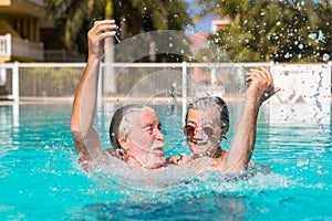Couple of two happy seniors having fun and enjoying together in the swimming pool smiling and playing. Happy people enjoying