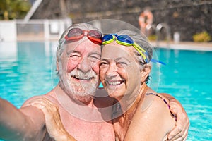 Couple of two happy seniors having fun and enjoying together in the swimming pool taking a selfie picture smiling and looking at