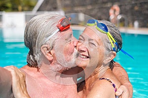 Couple of two happy seniors having fun and enjoying together in the swimming pool taking a selfie picture smiling and looking at