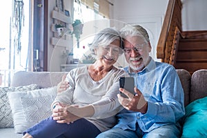 Couple of two old and mature people at home using tablet together in sofa. Senior use laptop having fun and enjoying looking at it