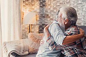 Couple of two old seniors hug together having fun and taking care each others at home on the sofa. Mature people in love enjoying