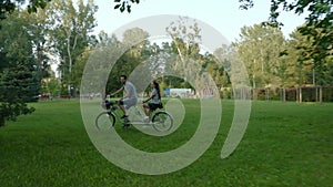 A couple on a two-seater tandem bike rides through the park between the trees