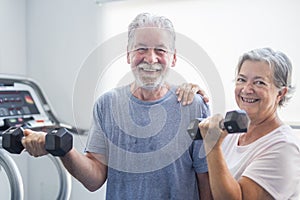 Couple of two seniors at the gym holding a dumbbells and with the tapirulan at the background - active mature people together