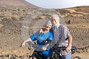 Couple of two seniors hugged together at the mountains riding their bikes - happy pensioners together looking at the camera with