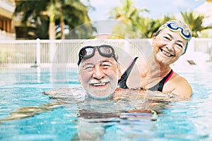 Couple of two seniors hugged in the water of swimming pool - active man and woman doing exercise together at the pool - hugged photo