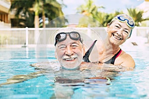 Couple of two seniors hugged in the water of swimming pool - active man and woman doing exercise together at the pool - hugged