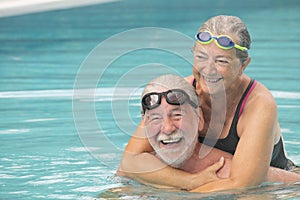 Couple of two seniors hugged in the water of swimming pool - active man and woman doing exercise together at the pool - hugged