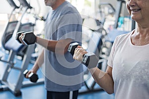 Couple of two seniors and mature people at the gym doing exercise - adults holding a dumbbell and working biceps together