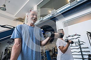 Couple of two seniors and mature people at the gym doing exercise - adults holding a dumbbell and working biceps together