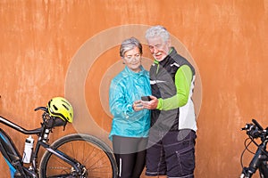 Couple of two seniors and mature people together married looking at the same phone with fitness clothes and with their bikes -