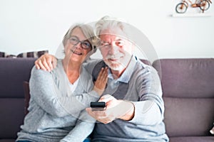 Couple of two seniors or mature people together on the sofa at home watching the tv or some film or serie - man holding the remote