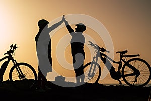 Couple of two seniors and mature people together at the sunset with their bikes giving five with the silhouette and the sea at the